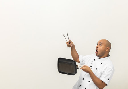 Young asian male chef in uniform cooking with iron grill pan and tongs kitchen utensil. Cooking man Occupation chef People in kitchen restaurant and hotel.の写真素材