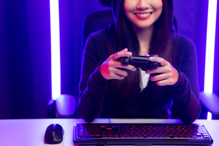 Playing video game. Young asian pretty woman sitting on chair holding joystick in living room. Happy...