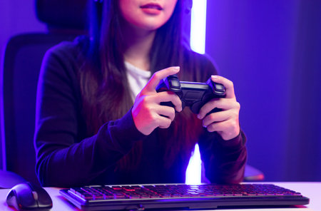 Close up hands Playing video game. Young pretty woman holding joystick controller console. Female Professional Streaming playing game online in dark room neon light.の写真素材