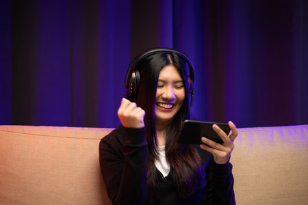 Playing video game on cellphone. Young asian pretty woman sitting on sofa holding smartphone in...