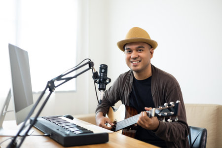 Professional Musician with condenser microphone and tablet for Mixing Mastering music. Hispanic male composing a song with guitar and piano keyboard at digital Recording home studioの写真素材