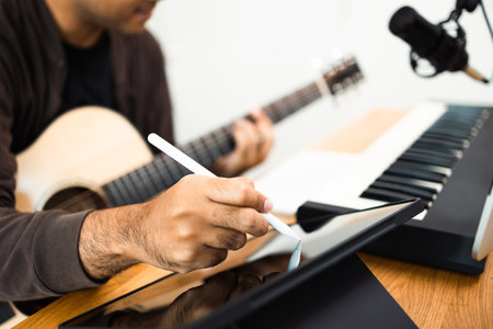 Close up hands song writer composing music note on tablet. Professional composer Recording Mixing and Mastering in home studio with keyboard and guitar. Digital music productionの写真素材
