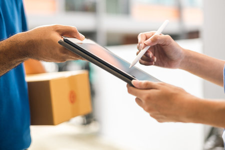 Hand woman signing electronic Signature on tablet for agreement of contract digital receiving parcel from blue delivery man from shopping online. Courier man delivering package to destination.の写真素材