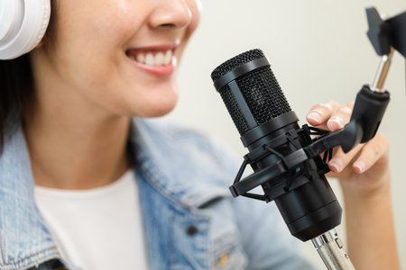 Content creator woman host streaming her a podcast on laptop with headphones and microphone interview cheering guest conversation at broadcast studio. Blogger motivation recording voice over radio.の写真素材