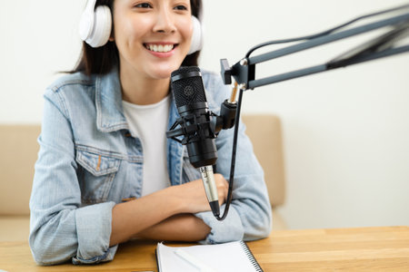 Content creator woman host streaming her a podcast on laptop with headphones and microphone interview cheering guest conversation at broadcast studio. Blogger motivation recording voice over radio.の写真素材