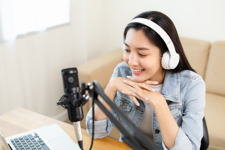 Content creator woman host streaming her a podcast on laptop with headphones and microphone...