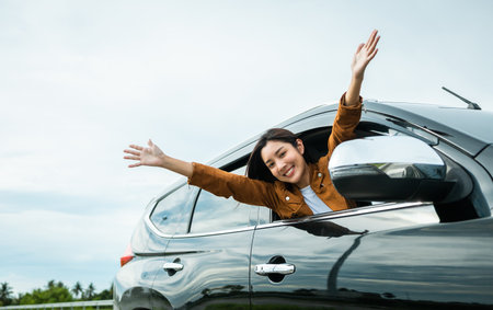 Young beautiful asian women getting new car. she very happy and excited. Smiling female driving vehicle on the road on a bright day. Sticking her head outta the windshieldの写真素材