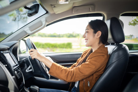 Young beautiful asian women getting new car. she very happy and excited. Smiling female driving vehicle on the road on a bright day.の写真素材