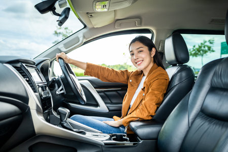 Young beautiful asian women getting new car. she very happy and excited. Smiling female driving vehicle on the road on a bright day.の写真素材