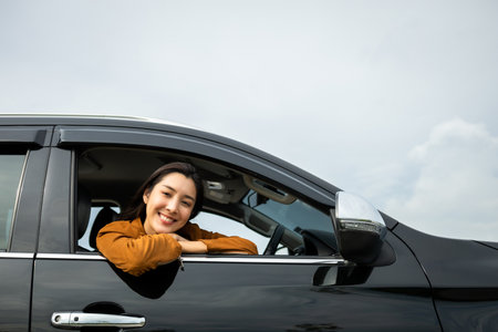 Young beautiful asian women getting new car. she very happy and excited. Smiling female driving vehicle on the road on a bright day. Sticking her head outta the windshieldの写真素材