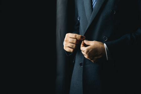 Confident businessman buttoning or adjust classic blue suit near window in hotel room at the morning. Handsome man wearing a nice suit on wedding day.の写真素材