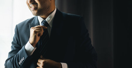 Confident businessman adjust classic blue suit with necktie near window in hotel room. Handsome man...