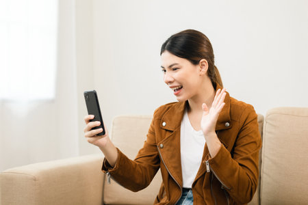 Beautiful young women using mobile phone sitting on sofa in living room. Using smartphone. Woman Shopping online store. Relax time at homeの写真素材