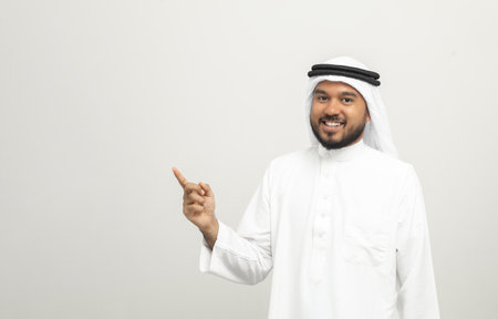 Portrait of arabic man with kandura dress on isolated white background. Arab business people showing hands gesture pointing to blank space.の写真素材