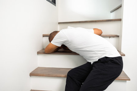A young man faints and collapses on the stairs of the house. He was injured in an accident and fell down the stairs. He was alone in the house not being helped by anyone. Broken boneの写真素材