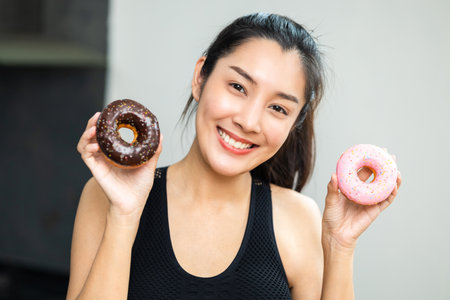 Beautiful female in sportswear eating Sweet donut dessert. Hungry Young woman holding chocolate donut unhealthy food. Food and dessert concept.の写真素材