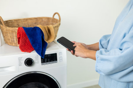 Close-up housewife Hand using mobile phone with applications operate Smart washing machine. Woman cleaning clothes controlled by technology smartphone.の写真素材