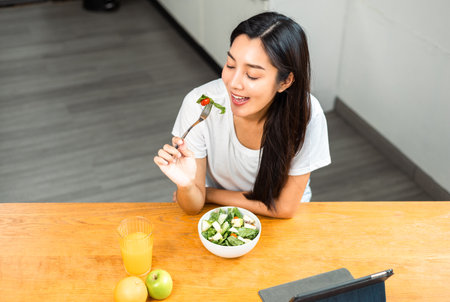 Young female eating organic greens vegetable salad in weight loss diet and wellness on table. Beautiful woman happily eat a healthy salad breakfast in kitchen in the morning. Diet food concept.の写真素材