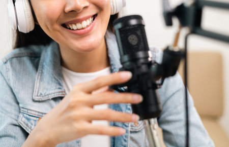 Content creator woman host streaming her a podcast on laptop with headphones and microphone interview cheering guest conversation at broadcast studio. Blogger motivation recording voice over radio.の写真素材