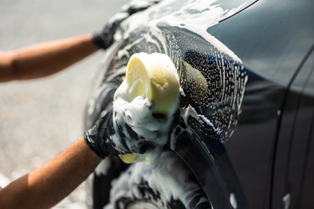 Man worker washing car service with foam and sponge. Car wash cleaning wipe station. Employees clean a vehicle professionally.の写真素材