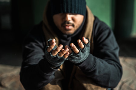 Poor tired stressed depressed hungry homeless man in the shadow city. Homeless man sitting on the street waiting for help food and money from people volunteer foundation donate.の写真素材