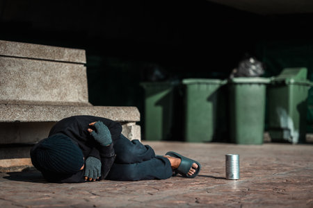 Poor tired stressed depressed hungry homeless man in the shadow city. Homeless man sitting on the street waiting for help food and money from people volunteer foundation donate.の写真素材