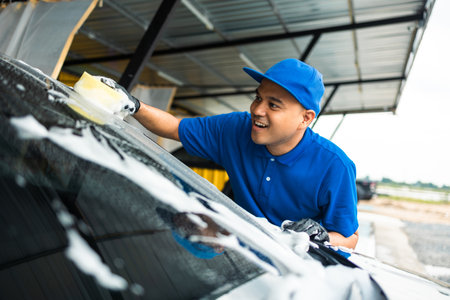 Man worker washing car service with foam and sponge. Car wash cleaning wipe station. Employees clean a vehicle professionally.の写真素材