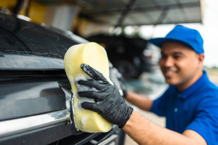 Man worker washing car service with foam and sponge. Car wash cleaning wipe station. Employees clean a vehicle professionally.の写真素材