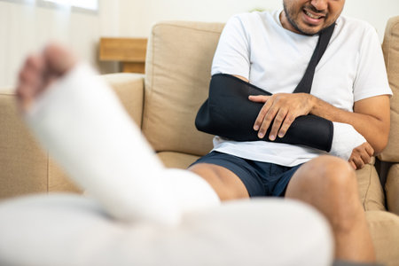 Man suffered pain from accident fracture broken bone injury with leg splints in cast neck splints collar arm splints sling support arm in living room. Social security and health insurance concept.の写真素材