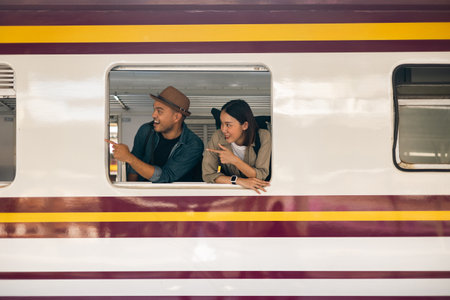 Couple asian traveller with bag on honeymoon travel by train Sticking head outta the window. Happy Man and woman near platform train station. Planning tourist on vacation time holiday weekend.の写真素材