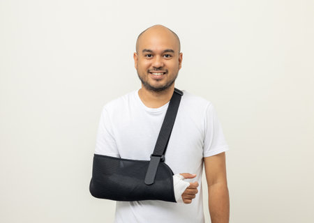 Happy young asian man broken arm on isolated background. Asian man put on plaster bandage cast splint. Male patient wearing sling support arm after accident injury. life insurance and accidentの写真素材