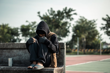 Poor tired stressed depressed hungry homeless man in the shadow city. Homeless man sitting on the street waiting for help food and money from people volunteer foundation donate.の写真素材