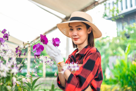Happy gardener woman in gloves plants flowers in greenhouse using tablet check growth quality of Plant. Florists woman working gardening in the backyard. Flower care harvesting.の写真素材