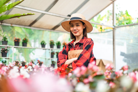 Happy gardener woman in gloves plants flowers in greenhouse using tablet check growth quality of Plant. Florists woman working gardening in the backyard. Flower care harvesting.の写真素材