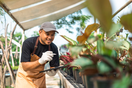 Happy gardener man in gloves plants flowers in greenhouse using tablet check growth quality of Plant. Florists man working gardening in the backyard. Flower care harvesting.の写真素材
