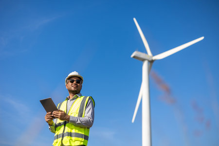 Engineer India man working with tablet at windmill farm Generating electricity clean energy. Wind...