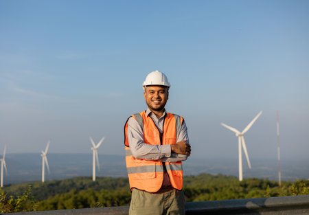 Engineer India man working at windmill farm Generating electricity clean energy. Wind turbine farm generator by alternative green energy. Asian engineer checking control electric powerの写真素材