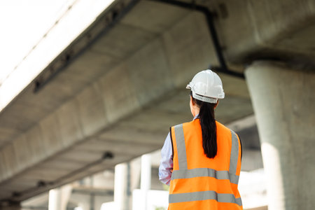 Asian engineer worker woman or architect looking construction with white safety helmet in construction site. Standing at highway concrete road site. Progress planning of highway bridge.の写真素材