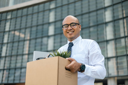 Employee first day working in the office. Happy Businessman with box cardboard personal item getting new jobs. Young man start working new office standing at building.の写真素材