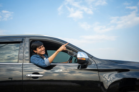 A young Asian man drives a car on a clear day. With beautiful blue sky. He smiling driving to travel by car. Sticking her head outta the windshieldの写真素材