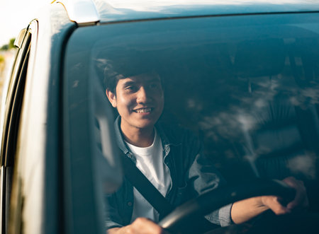 A young Asian man drives a car on a clear day. With beautiful blue sky. He smiling driving to travel by car. Sticking her head outta the windshieldの写真素材
