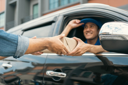 Asian delivery man with parcel in hand of blue uniform sending parcel to customer Sticking his head outta the windshield from shopping online service. Courier man send a package to destination.の写真素材