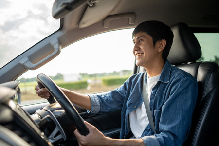A young Asian man drives a car on a clear day. With beautiful blue sky. He smiling driving to travel by car. Sticking her head outta the windshieldの写真素材