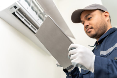 Technician in uniform using tablet to check list of maintenance and cleaning filters of air conditioner. Air condition maintenance service. Home services concept.の写真素材