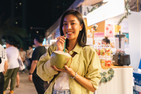 Asian women enjoy drinking coconut water street food at night market. Traveler Asian blogger woman...
