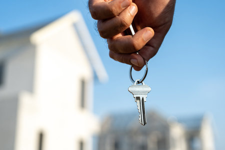 Close up male hand holding house key with sunlight. Real estate agent at construction site. New home purchase sales or rent. Choose Planning to buy propertyの写真素材