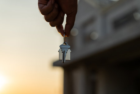Close up male hand holding house key with sunlight. Real estate agent at construction site. New home purchase sales or rent. Choose Planning to buy propertyの写真素材