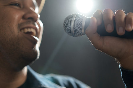 Close up shots of Attractive singer man singing music and playing guitar on stage with spotlight strike through the darkness at concert event. Musician performing live with light and smoke at hall.の写真素材