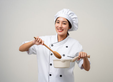 Young beautiful asian woman chef in uniform holding soup pot ladle utensils cooking in the kitchen various gesture menu good taste on isolated. Cooking woman chef people in kitchen restaurantの写真素材