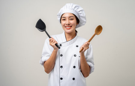 Young beautiful asian woman chef in uniform holding ladle utensils cooking in the kitchen various gesture delicious dish menu good taste on isolated. Cooking woman chef people in kitchen restaurantの写真素材